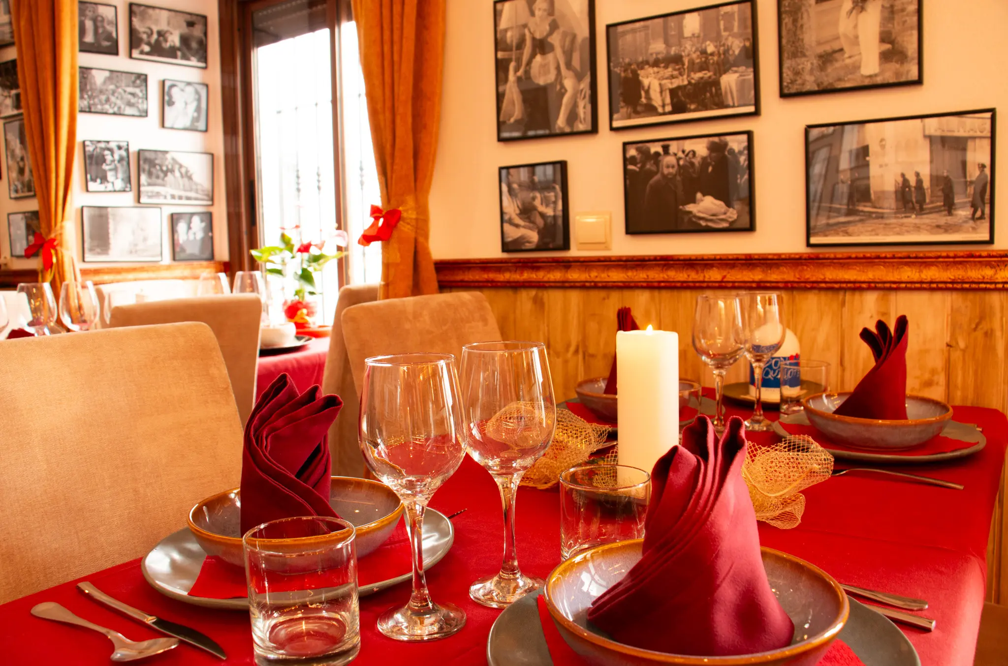 Mesa del restaurante Hostal Tolox con mantel rojo y decoración elegante, ideal para reservas con copas, platos y servilletas dobladas rodeadas de fotografías en blanco y negro.