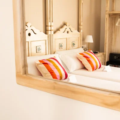 Reflejo en el espejo de una habitación del Hostal Tolox mostrando una cama doble, en un entorno acogedor y cuidado en la Sierra de las Nieves