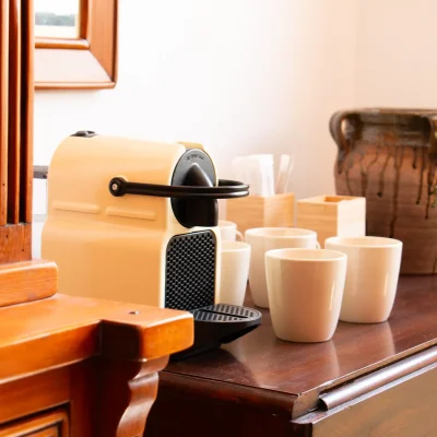 Zona común del Hostal Tolox con mesa de madera oscura, tazas blancas, cafetera y jarrón de arcilla, ideal para disfrutar de un café en un entorno relajado