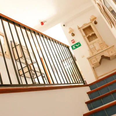Escaleras que conducen al pasillo de las habitaciones en el Hostal Tolox, con estanterías decorativas y ambiente acogedor andaluz